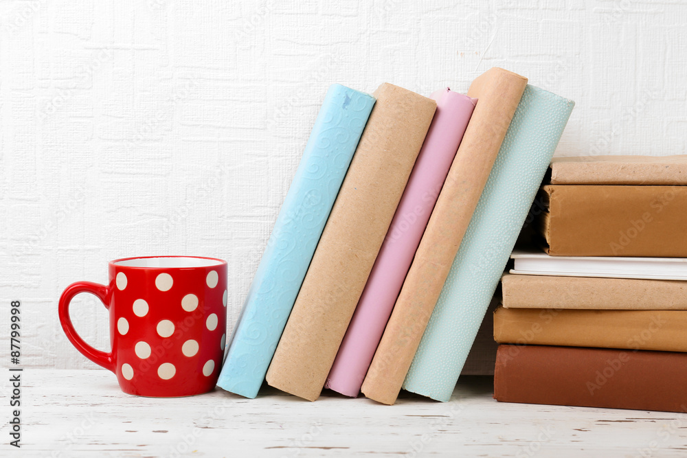 Books and cup on wooden shelf on wallpaper background