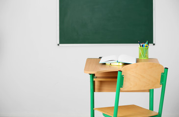 Wall Mural - Wooden desk with stationery and chair in class on blackboard background