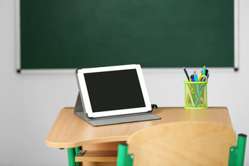 Wall Mural - Wooden desk with stationery and tablet in class on blackboard background