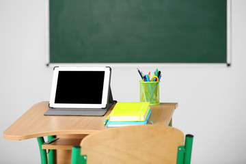 Canvas Print - Wooden desk with stationery and tablet in class on blackboard background