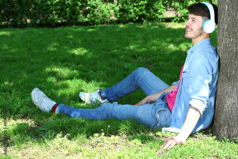 Man with headphones resting under tree in park