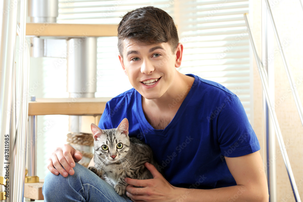 Handsome young man with cute cat sitting on steps at home