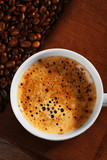 Fototapeta Boho - Cup of fresh coffee with beans on table, closeup