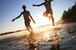 canvas print picture - Glückliche junge Menschen laufen und springen am See beim Sonnenuntergang