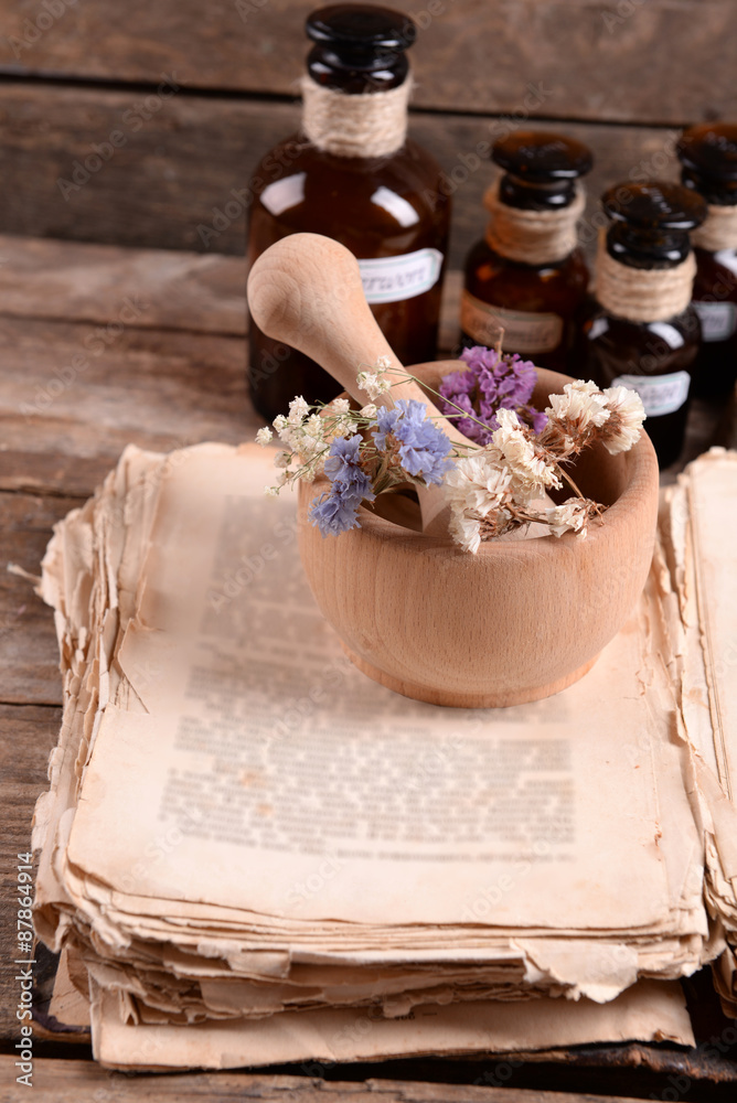 Old book with dry flowers in mortar and bottles on table close up