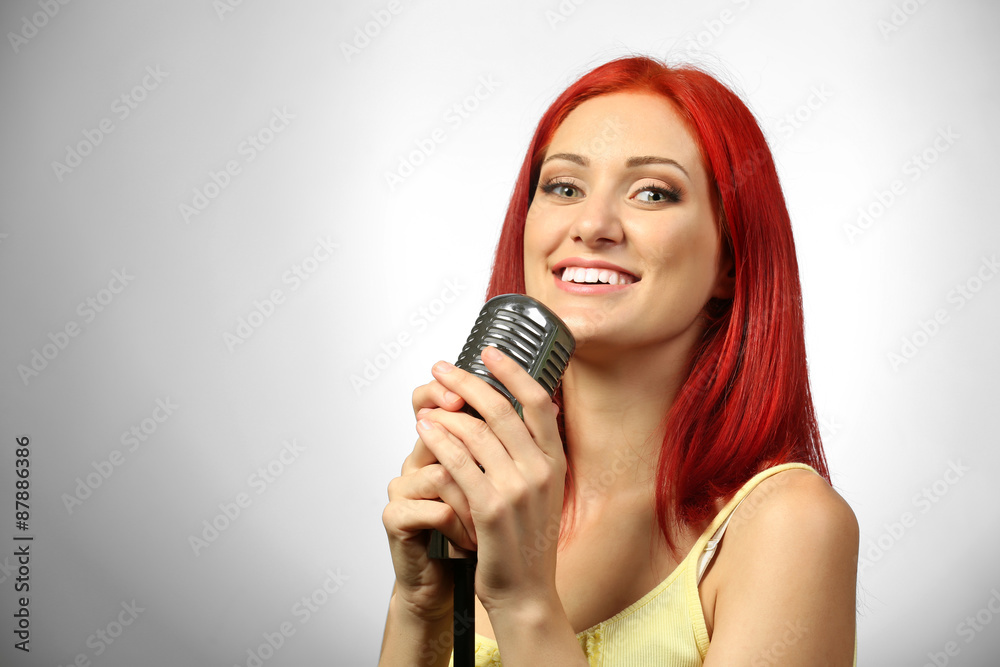 Beautiful young woman with microphone on gray background