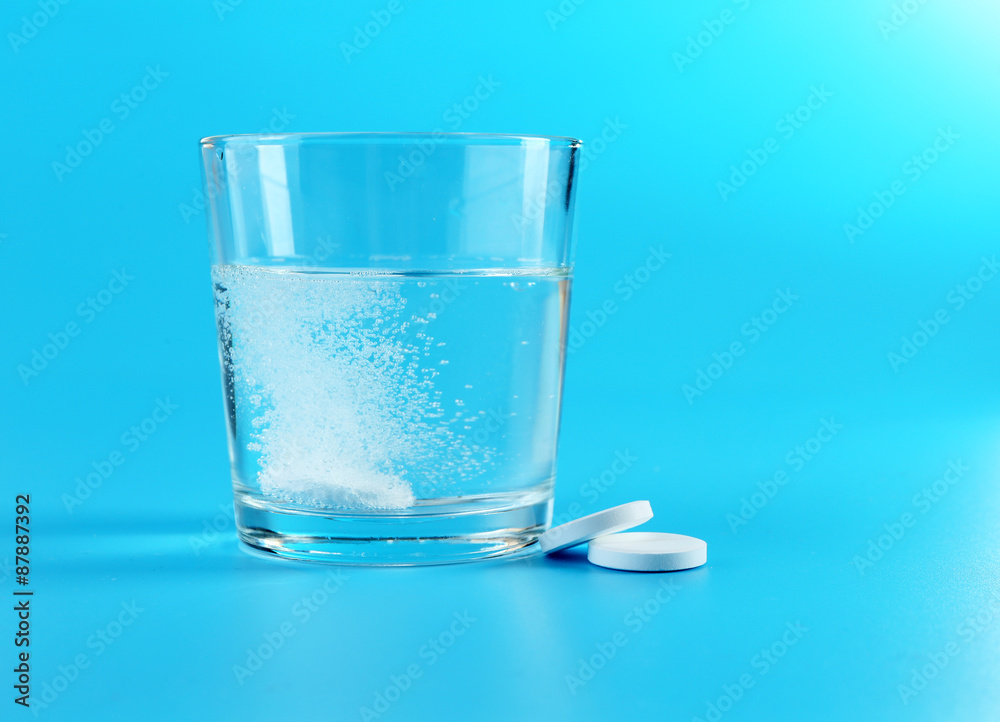 Glass of water and pills on blue background