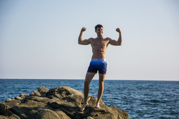 Wall Mural - Muscular young man on rock by sea