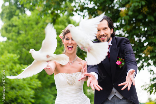 Fotografía Pareja de novios con vuelan palomas blancas en la boda