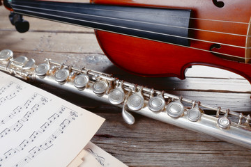 Wall Mural - Flute and violin with music notes on wooden table close up