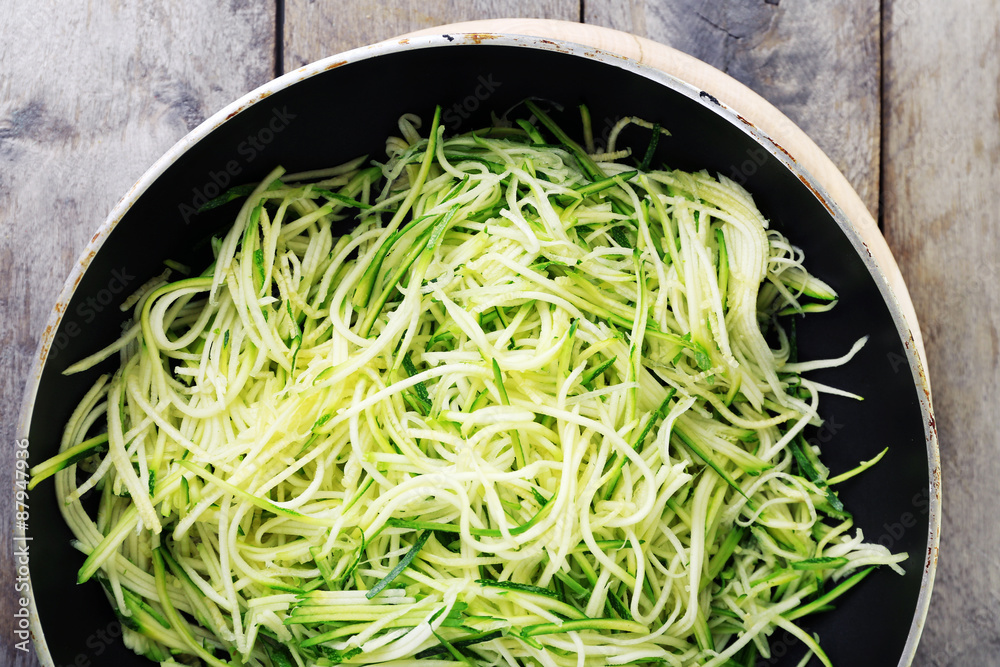 Grated zucchini and squash in pan on wooden table close up