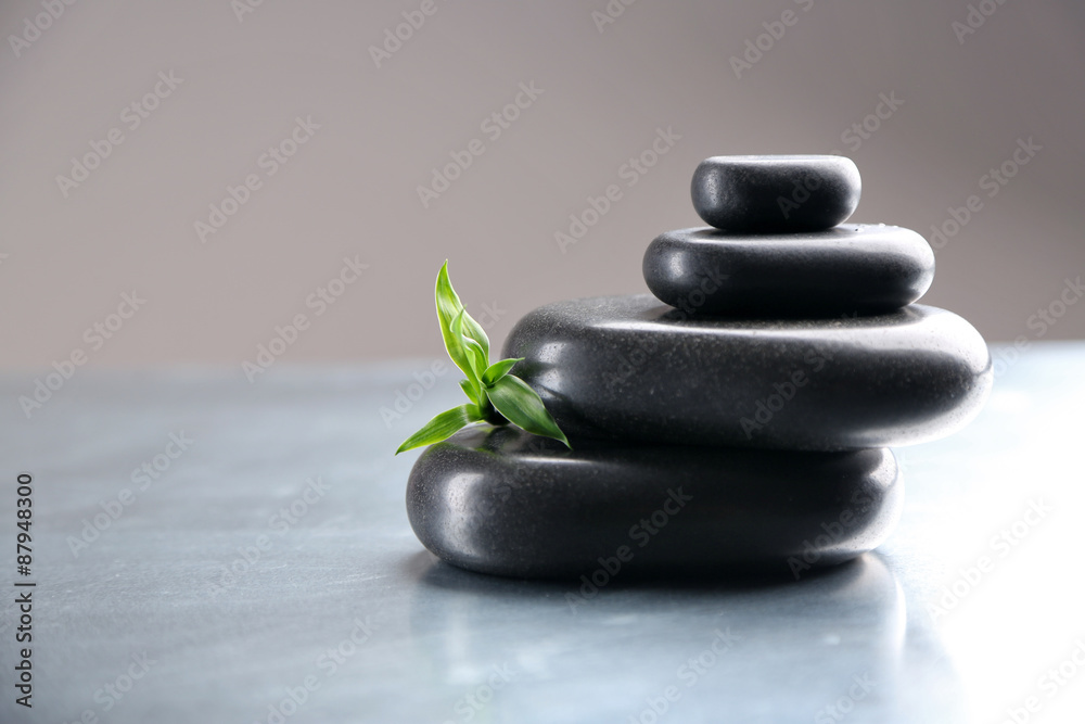 Stack of spa stones with green leaves on gray background