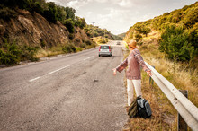 Angry And Disappointed Woman Hitchhiker With Straw Hat Opening Her Arms And Looking At The Cars Passing By Without Stopping