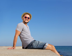 Sticker - Happy young man sitting by the sea in summer with hat