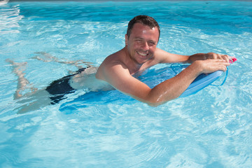 Wall Mural - Surfer man swim with his surf board in blue water swimming  and smile