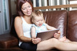 © Louis-Paul Photo - mother and baby are looking to play and read tablet computer on the couch at home