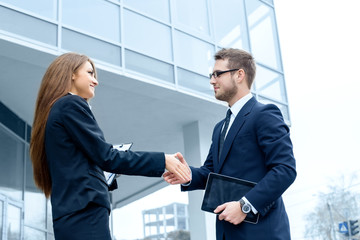 Business partners shaking hands, standing in front of his office.