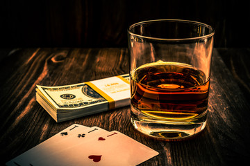 Wall Mural - Glass of whiskey and playing cards with pack of dollars on the wooden table