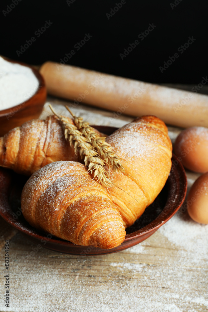 Fresh croissants with flour on wooden table on black background