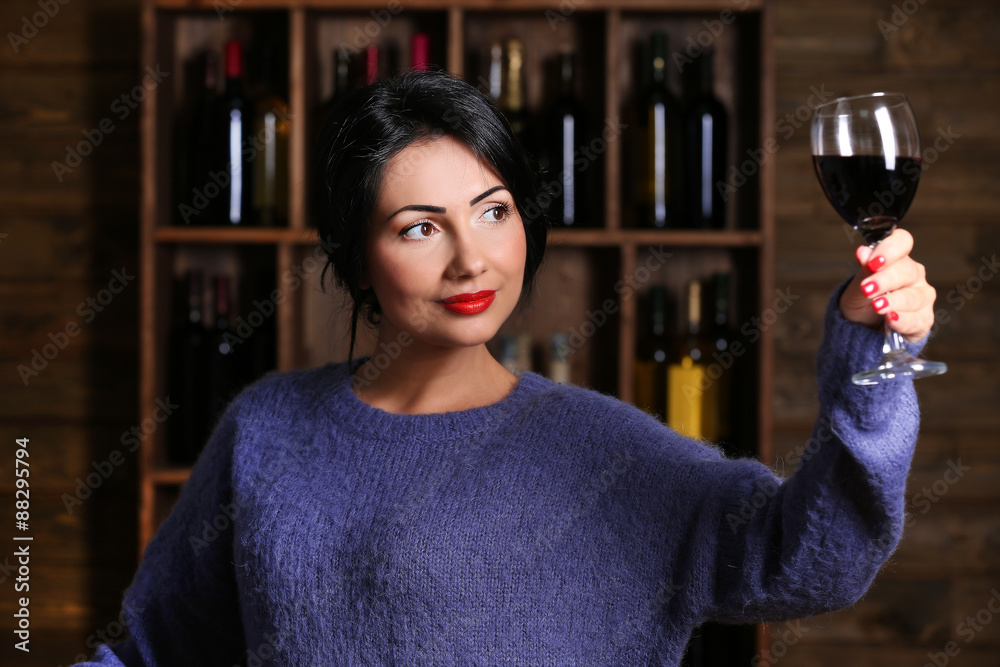Pretty young woman with wineglass on wine shelf background