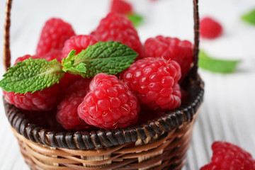 Wall Mural - Fresh red raspberries in wicker basket on wooden table, closeup