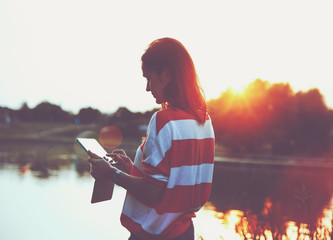 girl holding digital tablet pc at lake shore in sunrise light