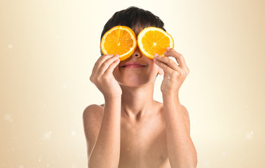 Child holding two slice oranges like glasses