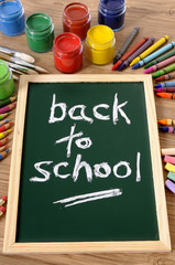 Canvas Print - Back to school word writing written on a small chalk blackboard on a student desk surrounded by pencils and crayons photo vertical