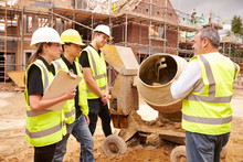 Builder Using Cement Mixer On Building Site With Apprentices