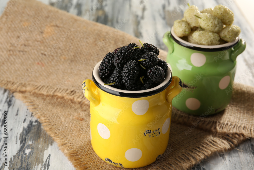 Ripe mulberries in watering cans on table close up