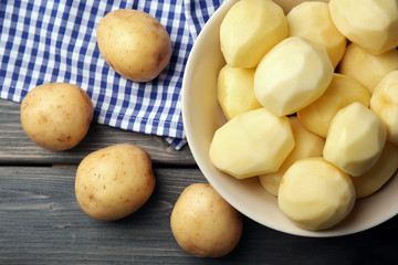 Peeled new potatoes in bowl on wooden table with napkin, top view