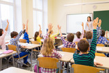 Fototapeta  - group of school kids raising hands in classroom