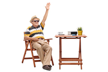 Canvas Print - Senior man sitting at a table and waving with hand