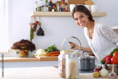 Fotografie, Obraz Young woman standing by the stove in the kitchen