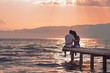 Rear view of a romantic young couple sitting on the pier enjoying  stunning sunset