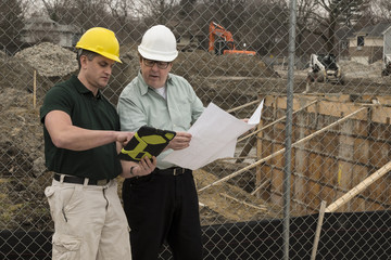 Two workers on a construction site using a tablet