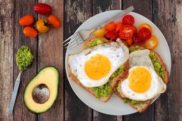 healthy avocado, egg open sandwiches on a plate with cherry tomatoes on rustic wood
