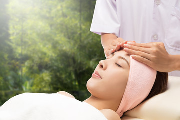 Relax beautiful woman face receiving massage with nature green background, asian spa and beauty, enjoying a facial massage.