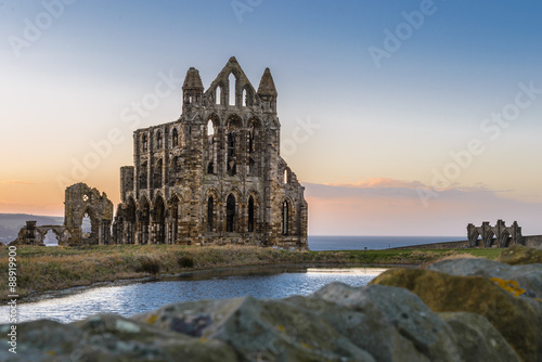 Fotografie, Obraz Stone ruins of Whitby Abbey on the cliffs of Whitby, North Yorkshire, England at sunset