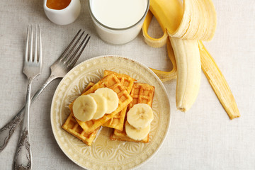 Poster - Sweet homemade waffles with sliced banana on plate, on light background