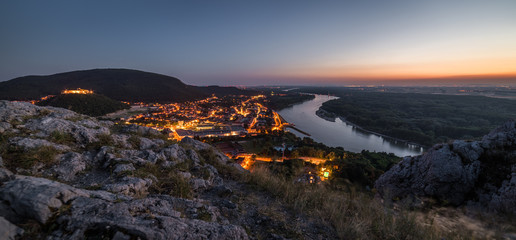 Wall Mural - View of Lit Small City with River from the Hill at Sunset