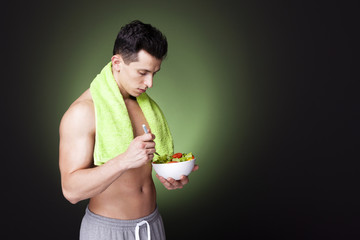 Young fitness man holding a bowl of fresh salad on dark backgrou