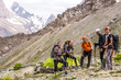 © alexbrylovhk - Alpine climbers team and camp Group of five people men and women staying along green camping tent on majestic mountain landscape of deserted Asian area