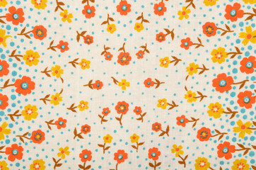 Small floral pattern on fabric. Yellow and orange flowers with blue dots print as background.