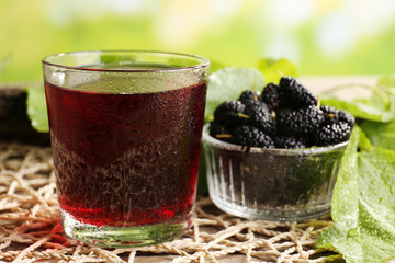 Wall Mural - Glass of refreshing mulberry juice with berries on bright background