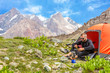 Traveling man eating meal.
Hiker sitting in his orange camping tent and having lunch stove and cooking gear mountain landscape on background