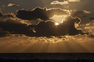 Puesta de sol con nubes y con velero en el horizonte.