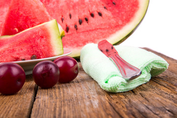 slices of watermelon on the plate next with plums on a wooden ba