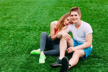 Wall Mural - Young athletic couple sitting on the grass