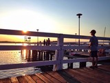 Fototapeta Pomosty - Chłopiec na molo patrzy na zachód słońca